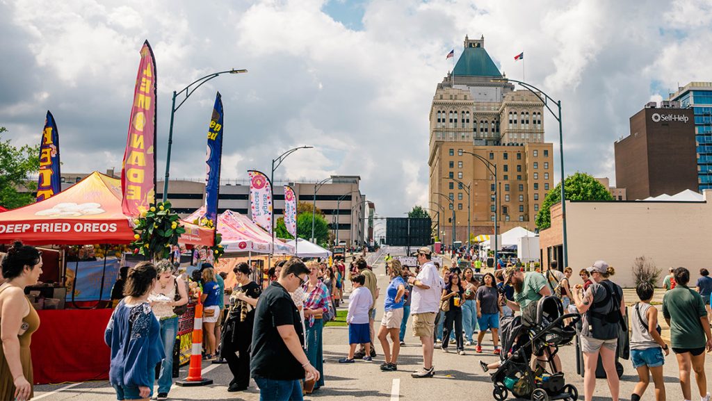 Downtown Greensboro during Folk Fest with streets lined with food trucks and tents and people filling the streets.