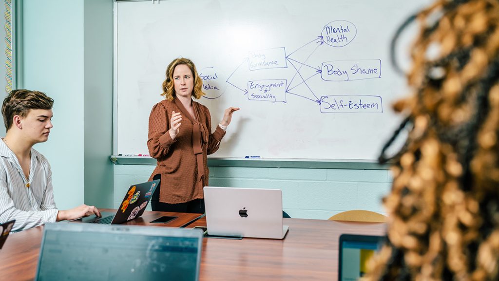 UNCG Professor Michaeline Jensen writes on a whiteboard in front of students.