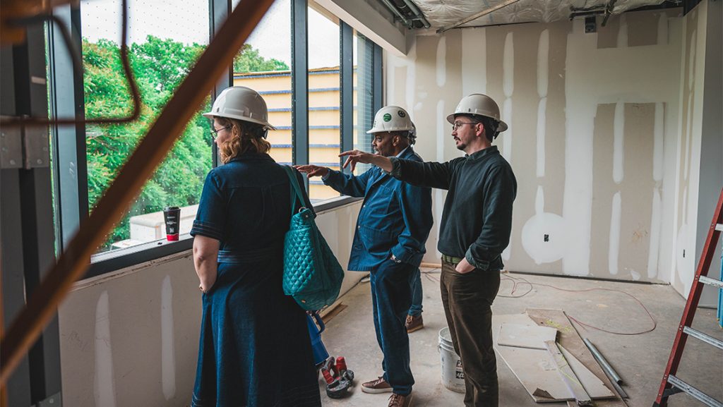 People wearing hard hats point out a window.